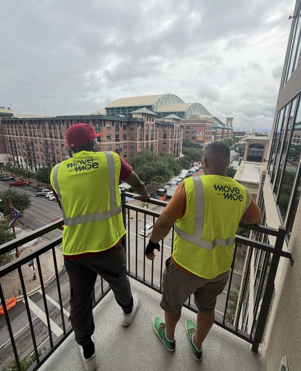 Two movers on an apartment balcony overlooking Houston