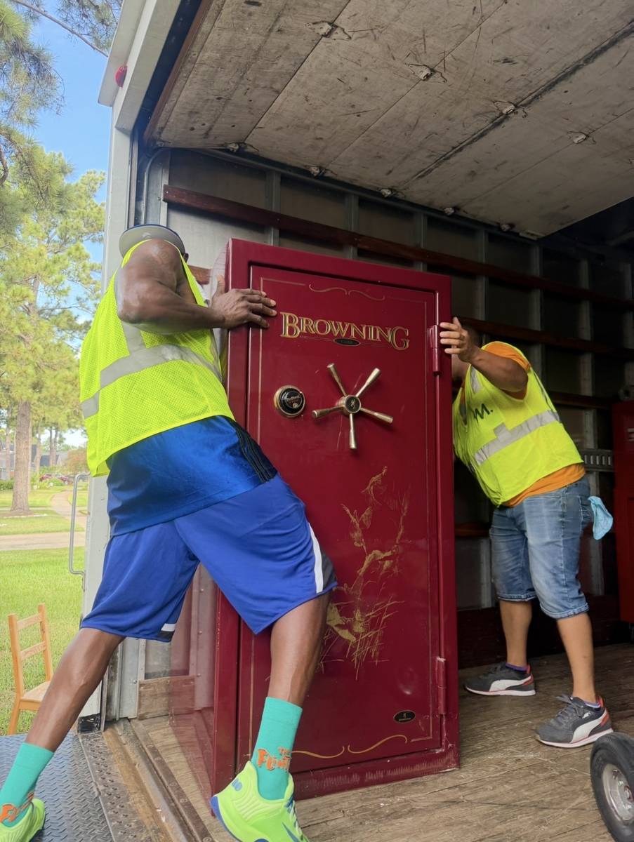 Two movers carefully lifting a heavy safe out of the truck