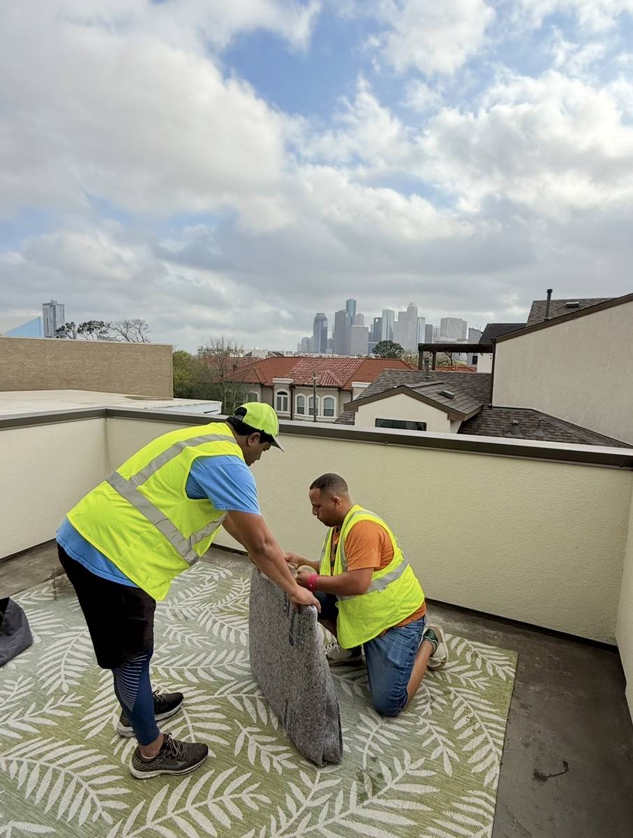 Two movers wrapping furniture on a rooftop patio