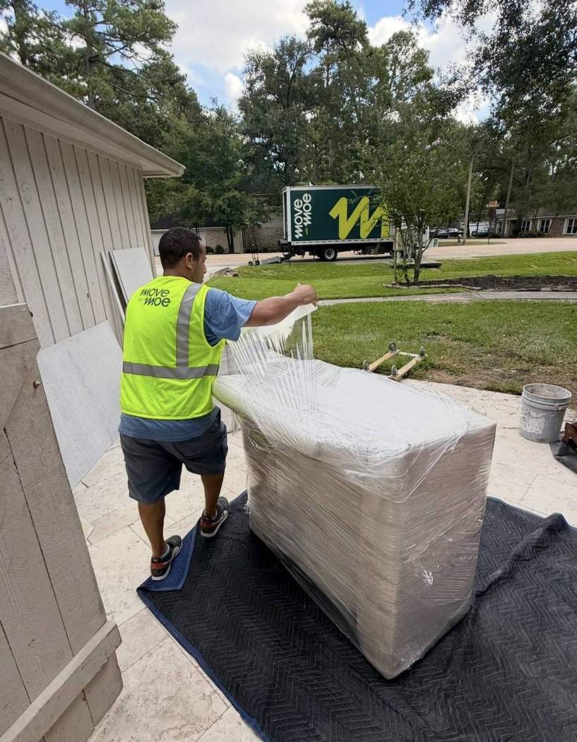 A mover with a fully wrapped sofa outside a home