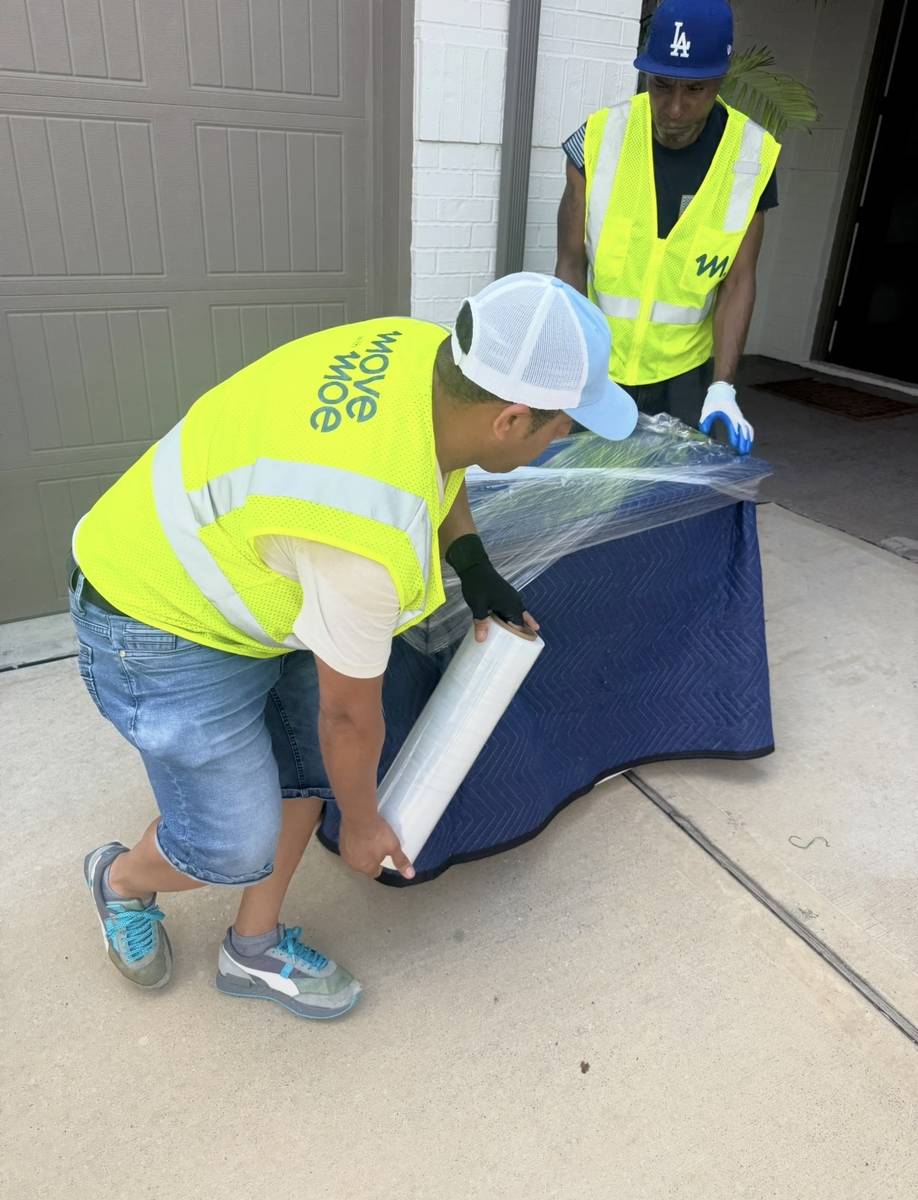 Movers wrapping a table in plastic before loading