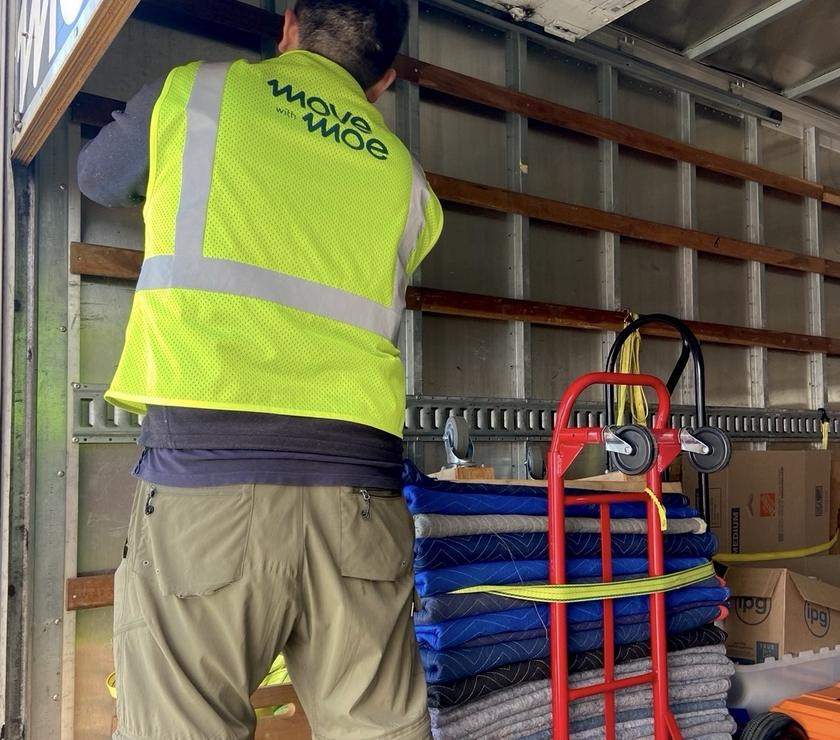 A mover loading a dolly and moving blankets onto the truck