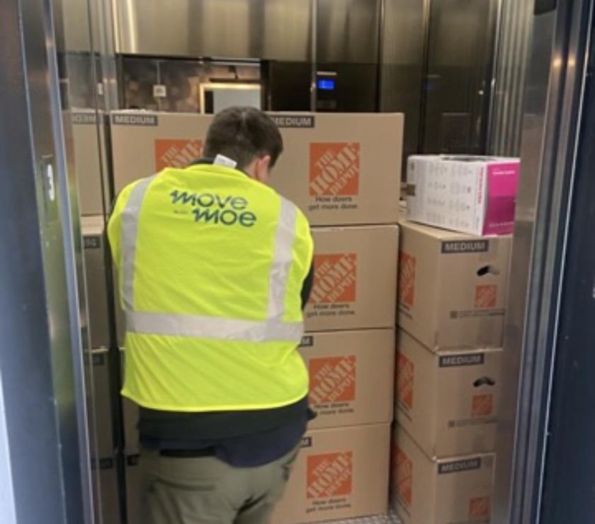 A mover bringing a stack of boxes up in a building elevator
