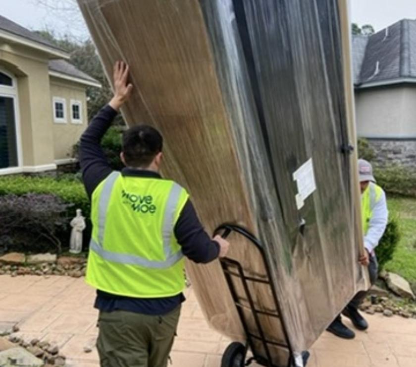 Two movers rolling wrapped furniture out of a home